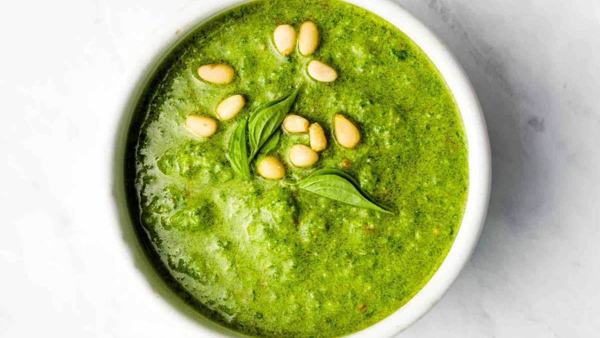 Green pesto in a white bowl with pine nuts.
