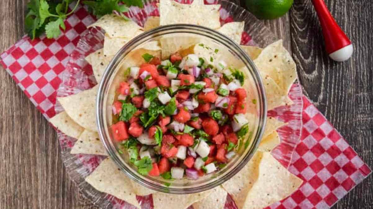 A bowl of watermelon salsa on a red and white checkered tablecloth.