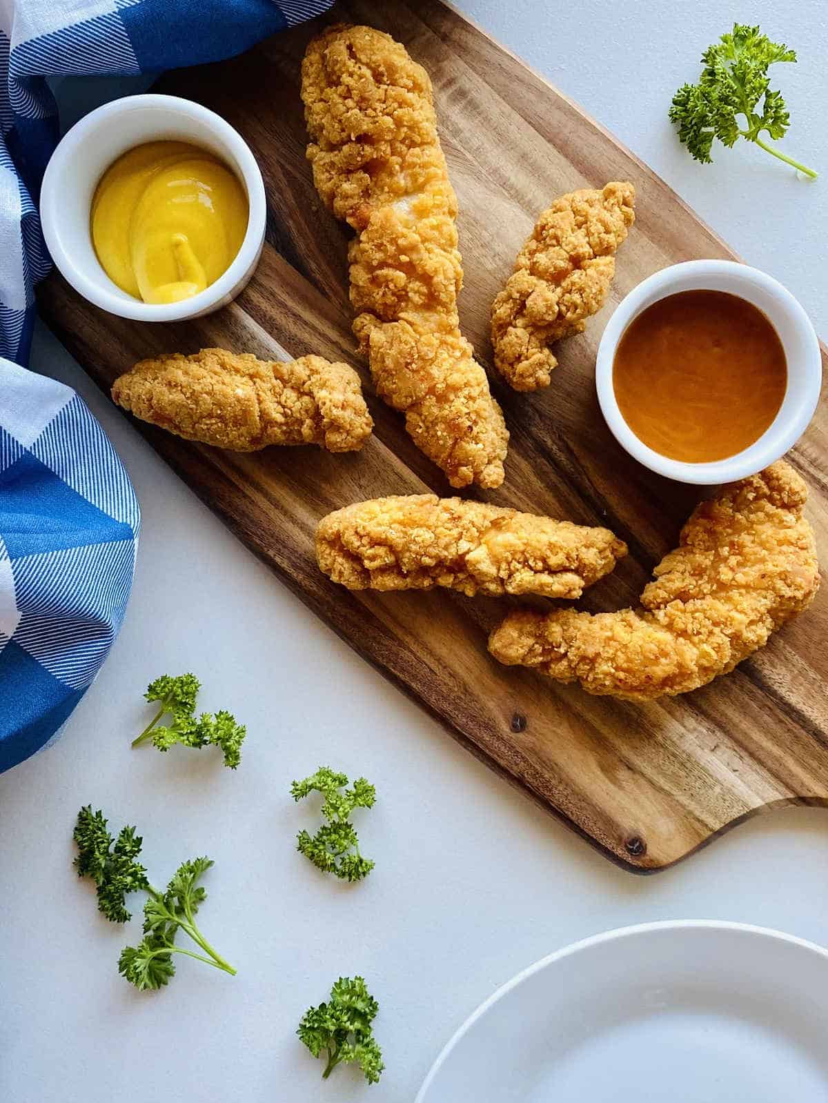 Savory chicken tenders plated on a rustic wooden cutting board, accompanied by an array of delectable sauces.