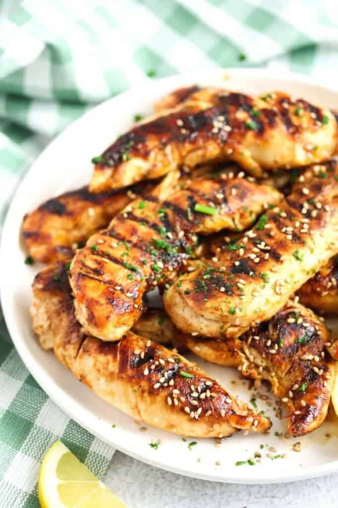 Grilled chicken tender recipes with sesame seeds and lemon wedges on a plate.