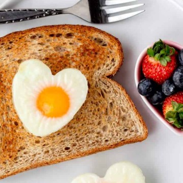 A plate of toast with a heart shaped egg and berries.