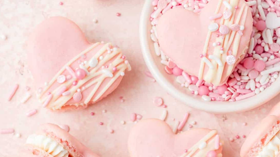 Valentine's day macarons on a pink background with sprinkles.