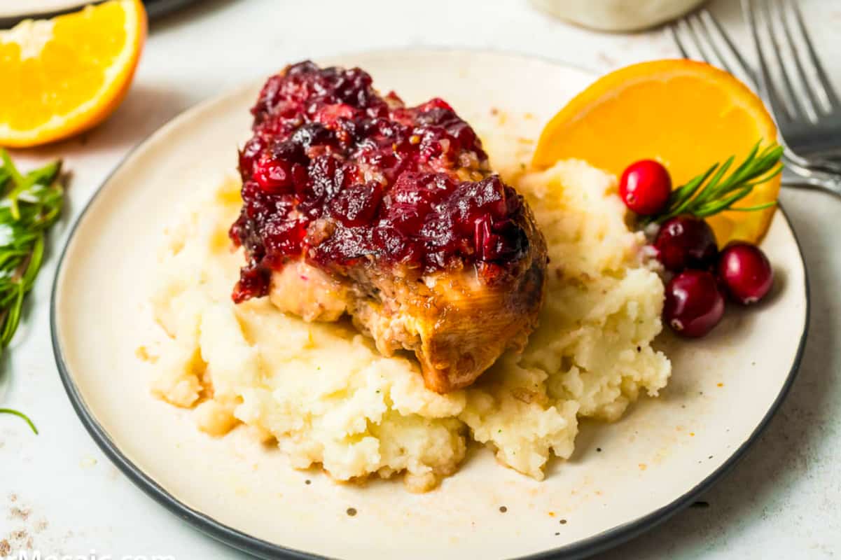 Cranberry chicken on a plate with mashed potatoes and oranges.