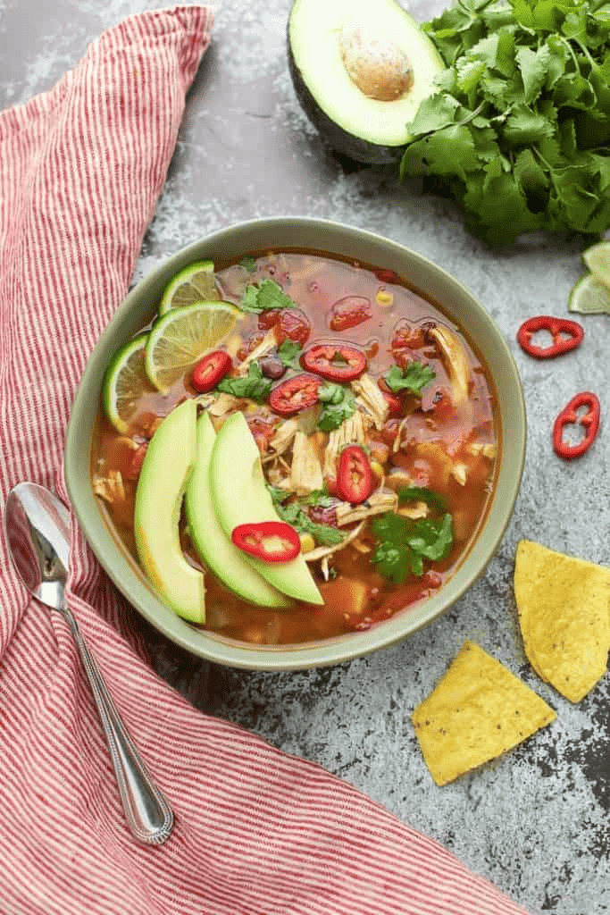 A bowl of mexican chicken soup with avocado and tortilla chips.