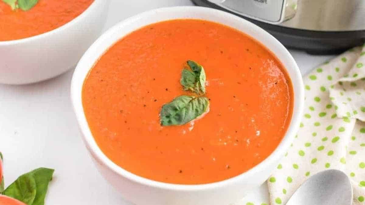 A bowl of tomato soup with basil in front of an instant pot.
