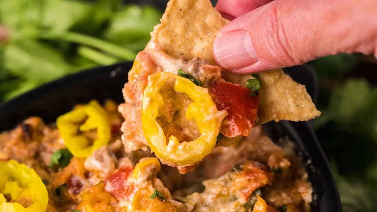 A hand is dipping a tortilla into a bowl of mexican dip.
