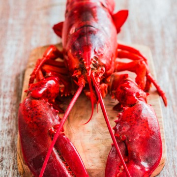 A red lobster is sitting on a wooden cutting board.