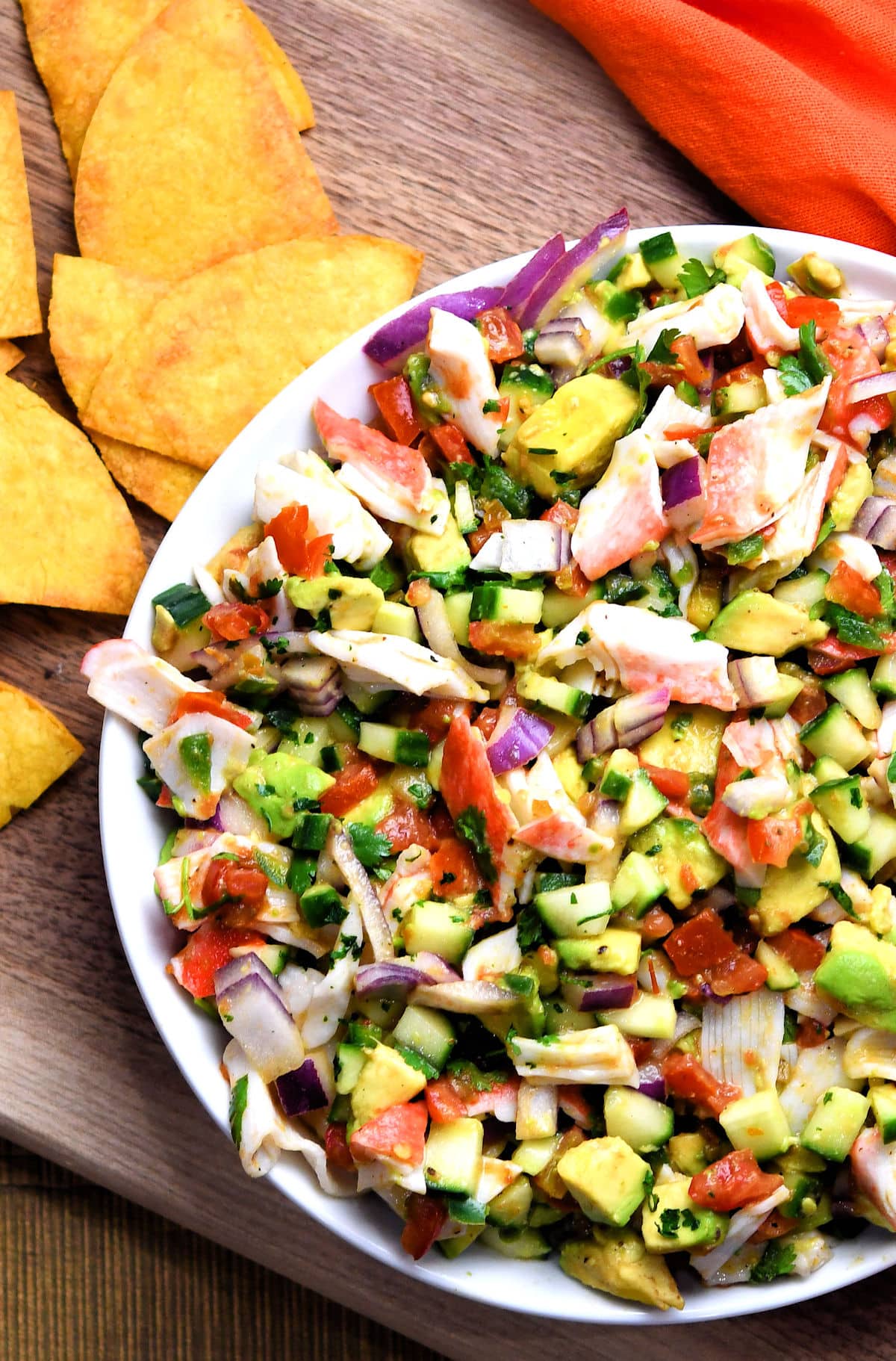 A bowl of salsa with tortilla chips on a wooden cutting board, perfect for accompanying imitation crab recipes.