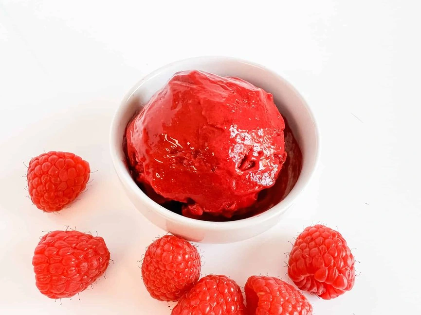 A bowl of raspberry sorbet surrounded by raspberries.