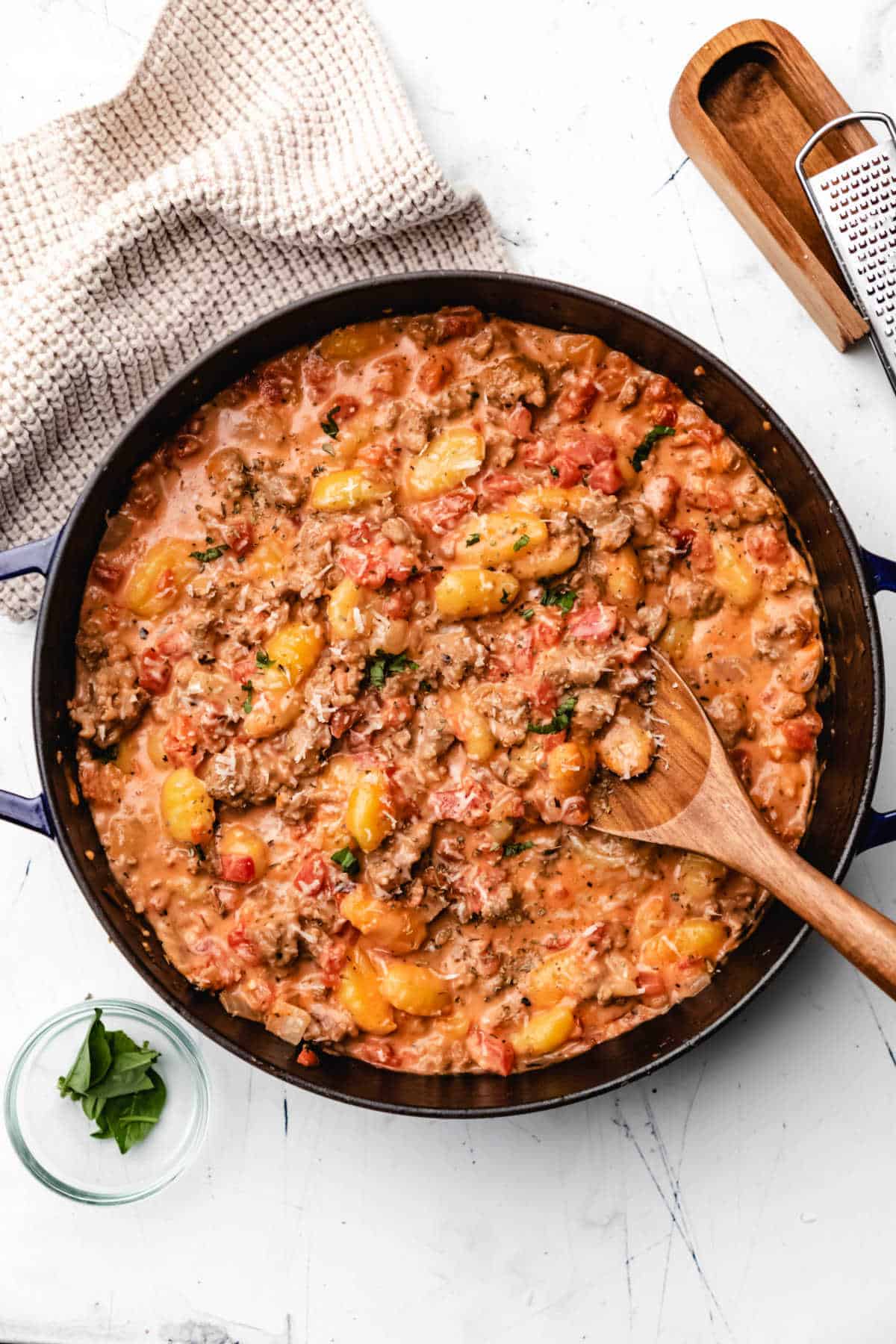 A skillet full of ground sausage and tomato stew with a wooden spoon.