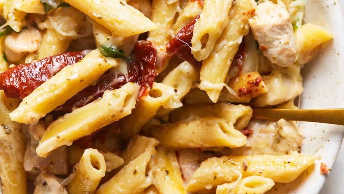 Penne pasta with chicken and parsley in a white bowl.