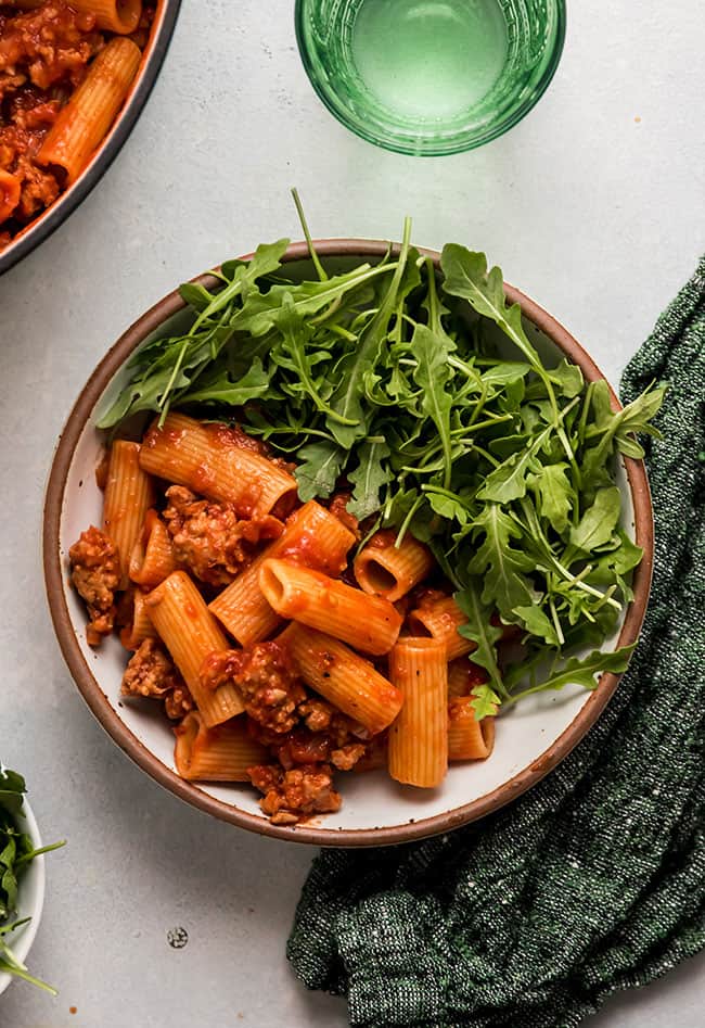 A flavorful bowl of pasta with meaty and delicious ground sausage sauce, topped with a generous serving of nutritious greens.