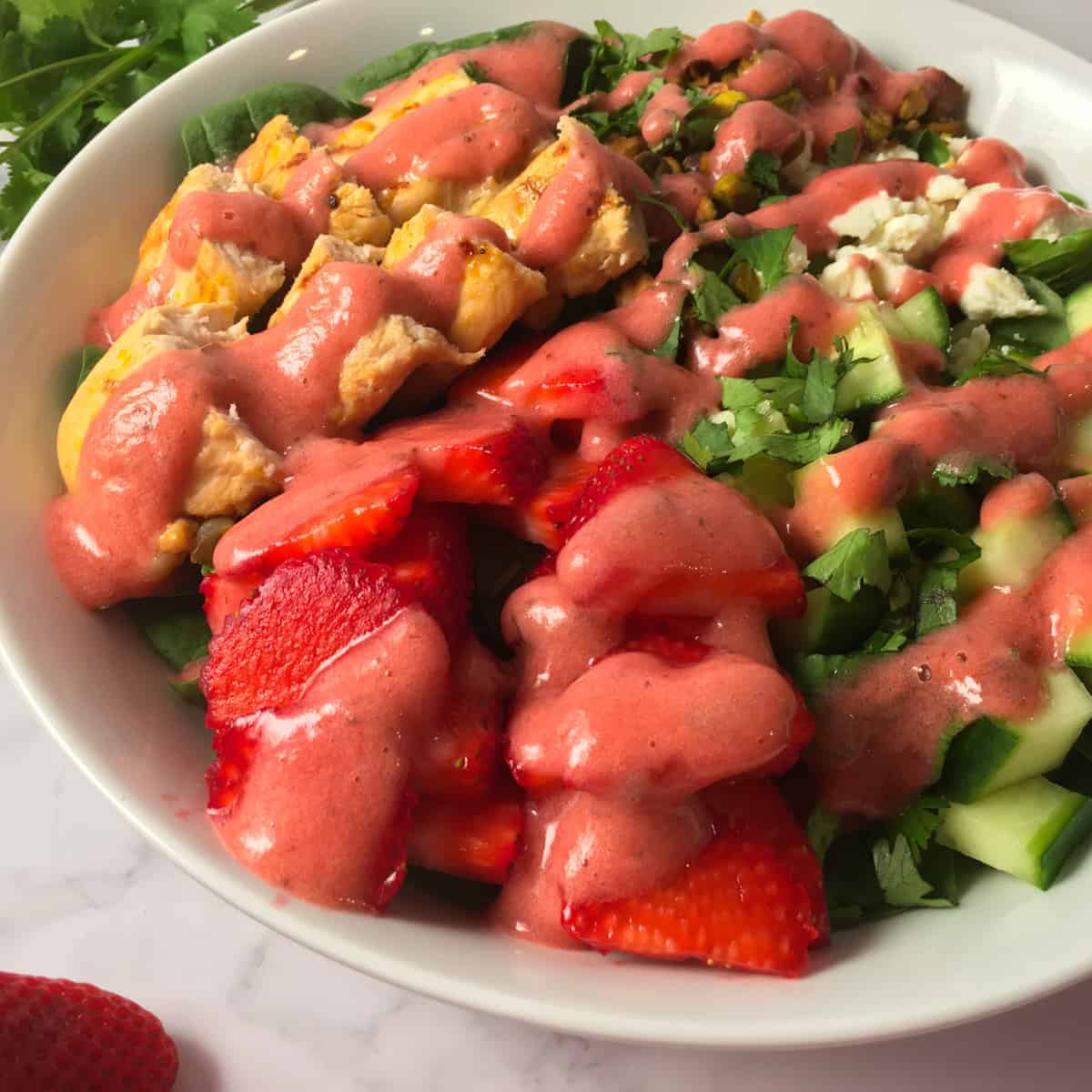A bowl of salad with strawberries and dressing.