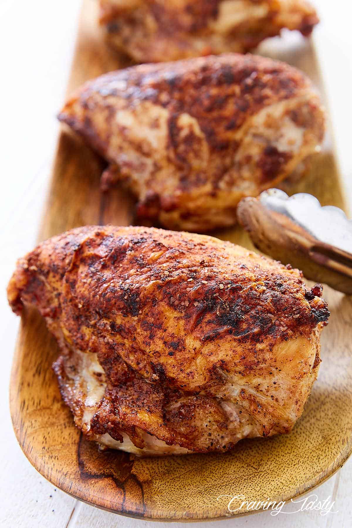 Three bone-in chicken breasts on a wooden plate.