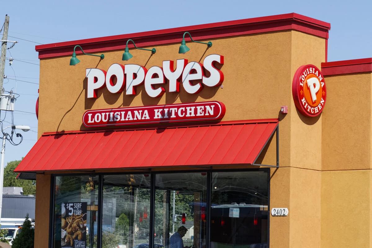Exterior view of a Popeyes Louisiana Kitchen restaurant with a red roof, large logo signage, and a Louisiana Kitchen emblem on the wall, welcoming guests to discover favorites like those featured on the Popeyes gluten free menu.