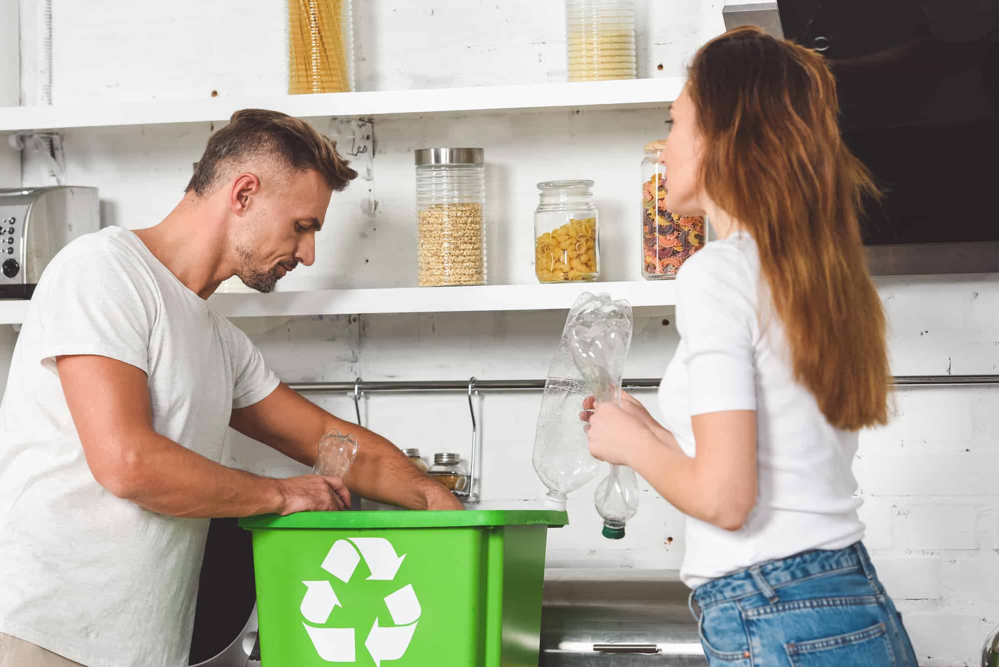 A man and woman standing next to a recycling bin.