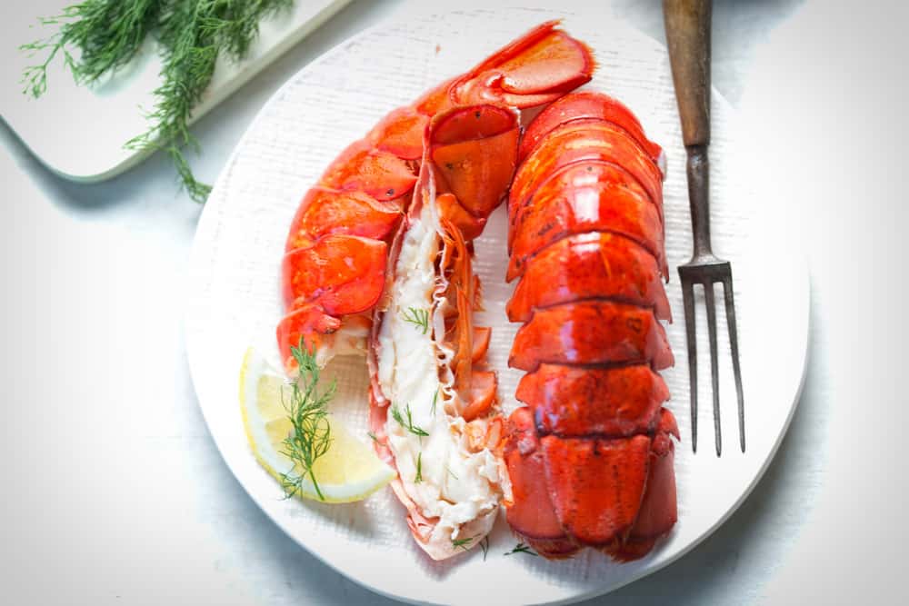 Two lobsters on a plate with lemon and dill.
