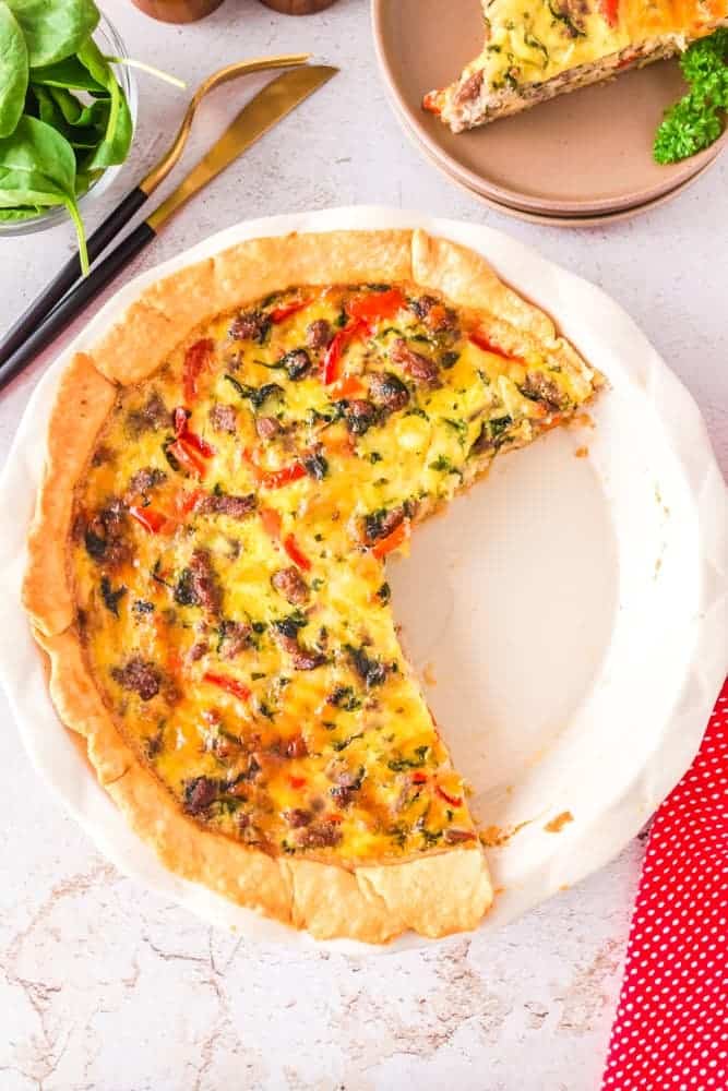 A delicious quiche with a slice taken out of it, featuring flavorful ground sausage.