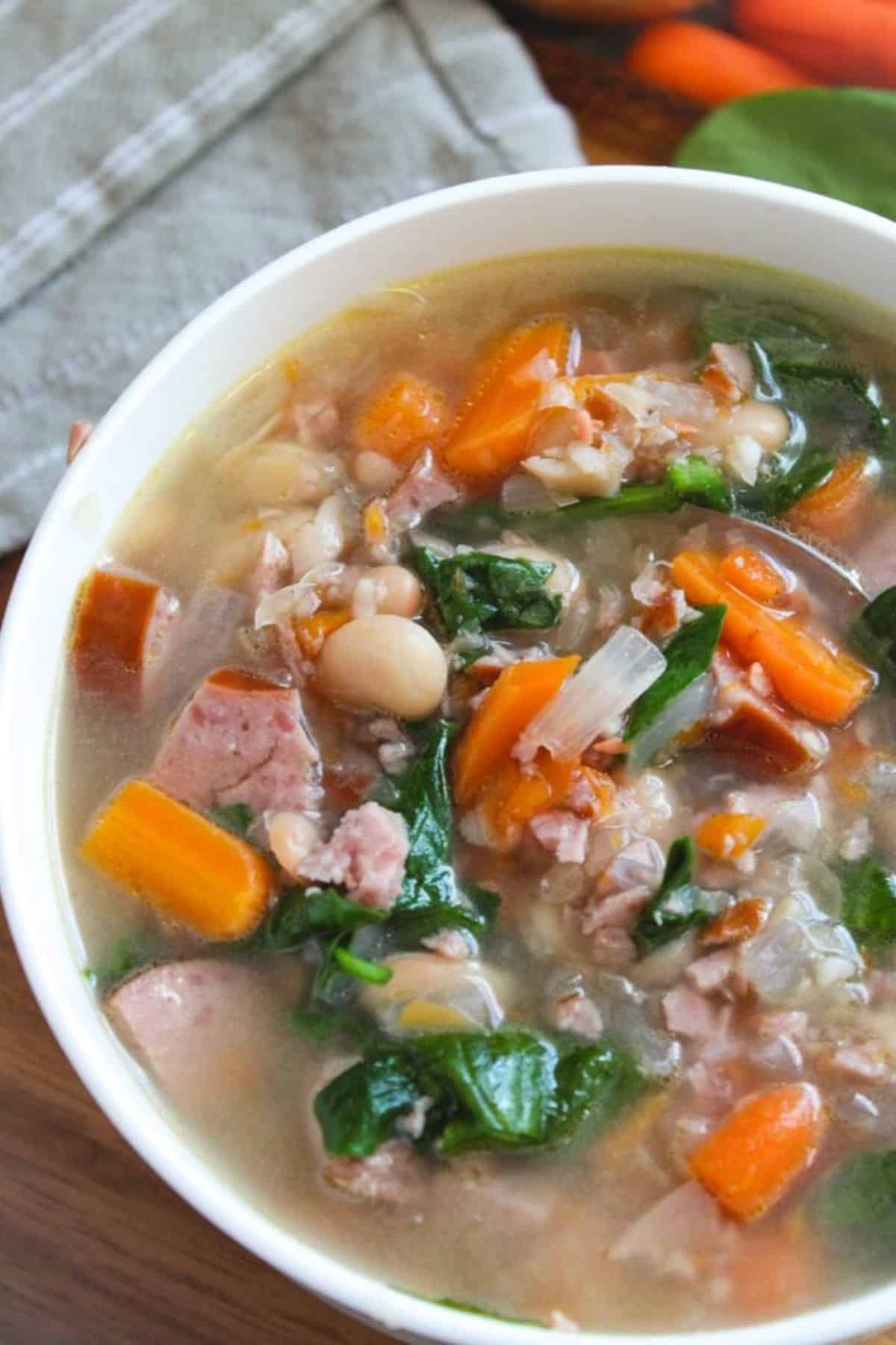 A hearty bowl of sausage and bean soup with carrots and spinach.