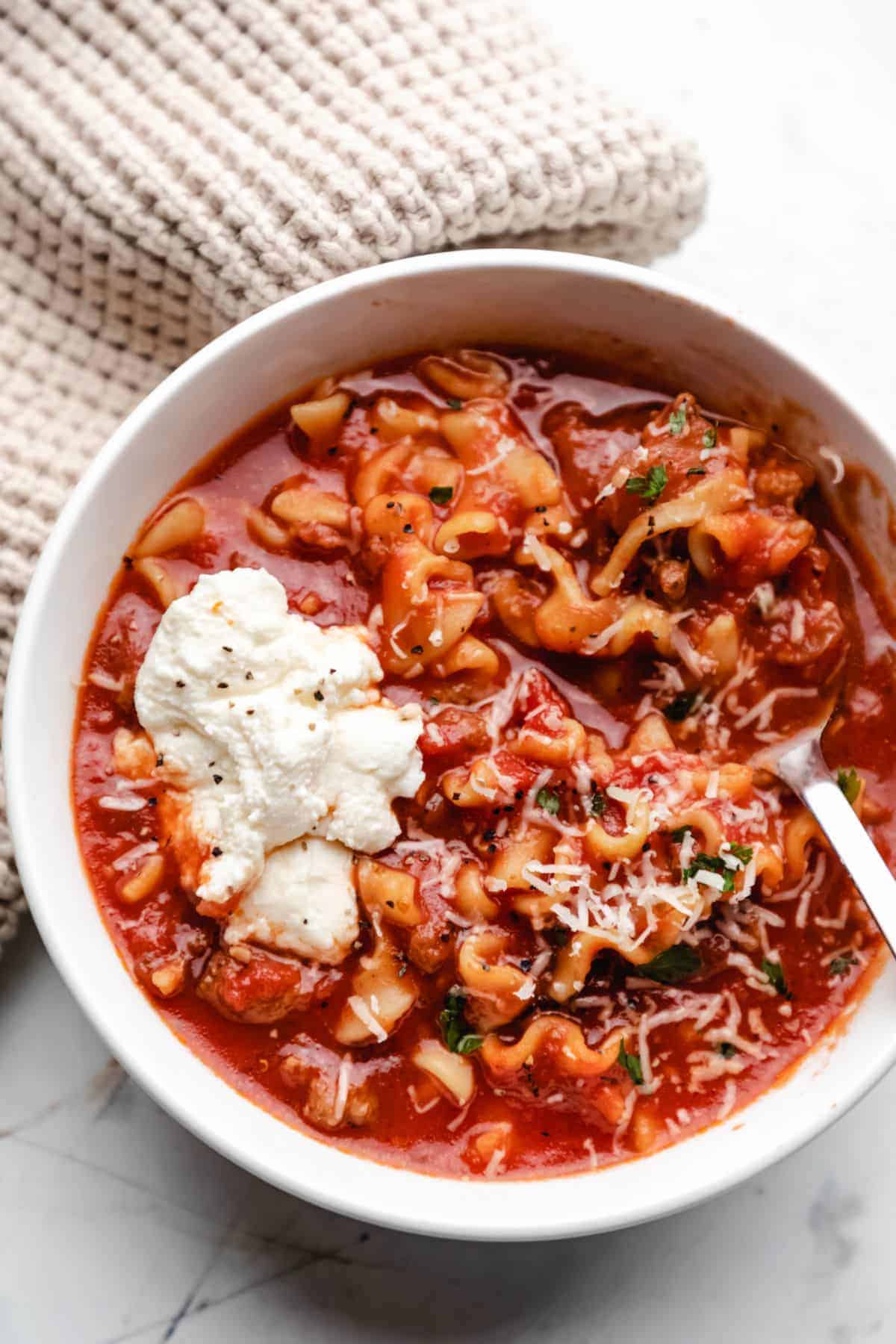 A bowl of tomato soup with sour cream and sausage.