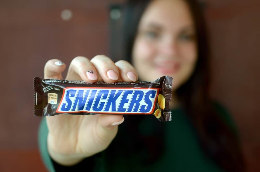 A woman holding up a snickers bar.