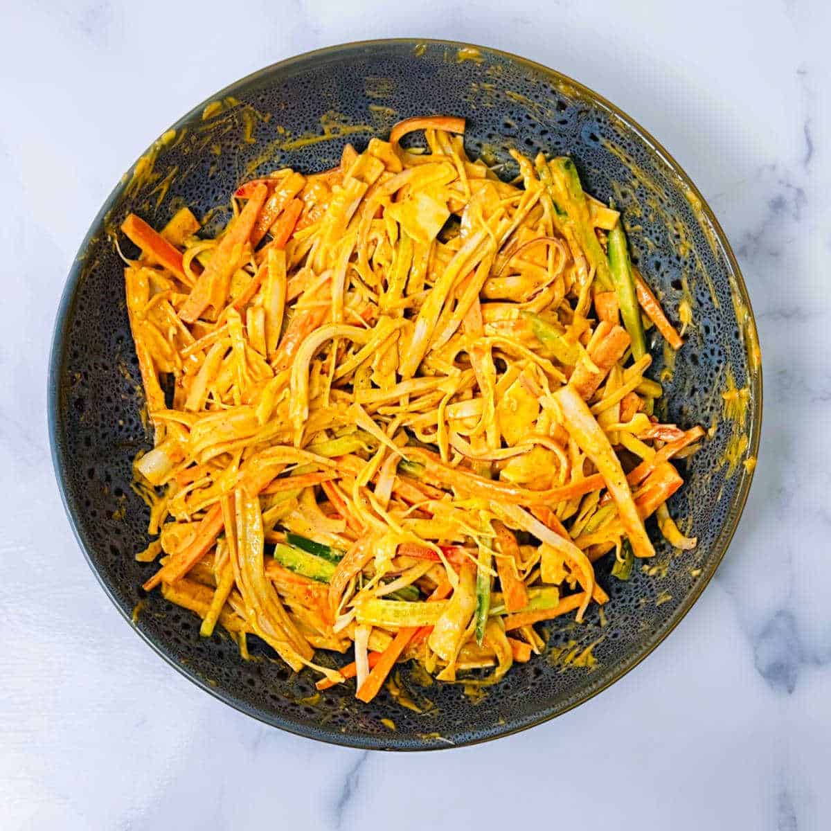 Shredded carrots in a bowl on a marble counter, perfect for your imitation crab recipes.
