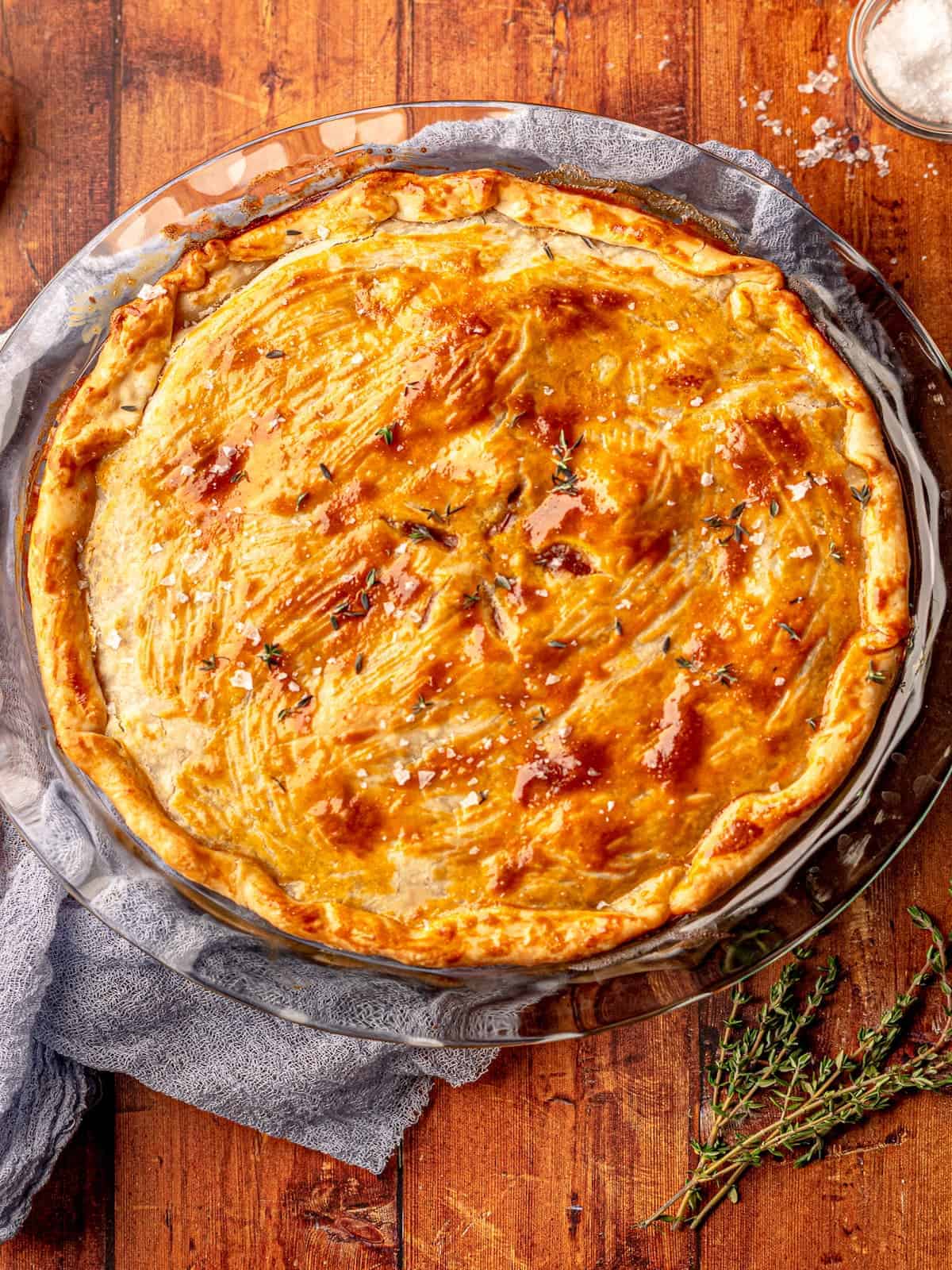 A quiche, topped with a savory chuck steak filling, is elegantly presented on a wooden table.