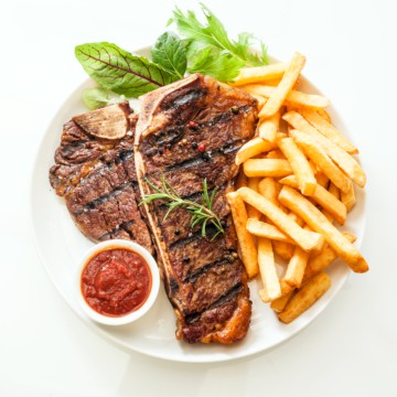 A mouthwatering steak, cooked to perfection, served with a generous portion of golden crispy fries and topped with a delectable sauce. Presented on a pristine white plate.