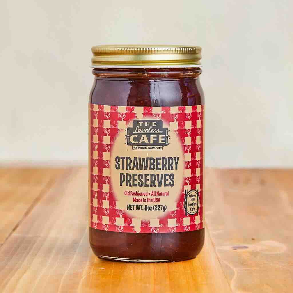 A jar of strawberry preserves on a wooden table.