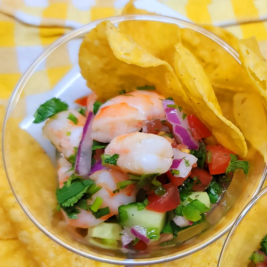 A bowl of shrimp salsa with chips on a yellow checkered tablecloth.