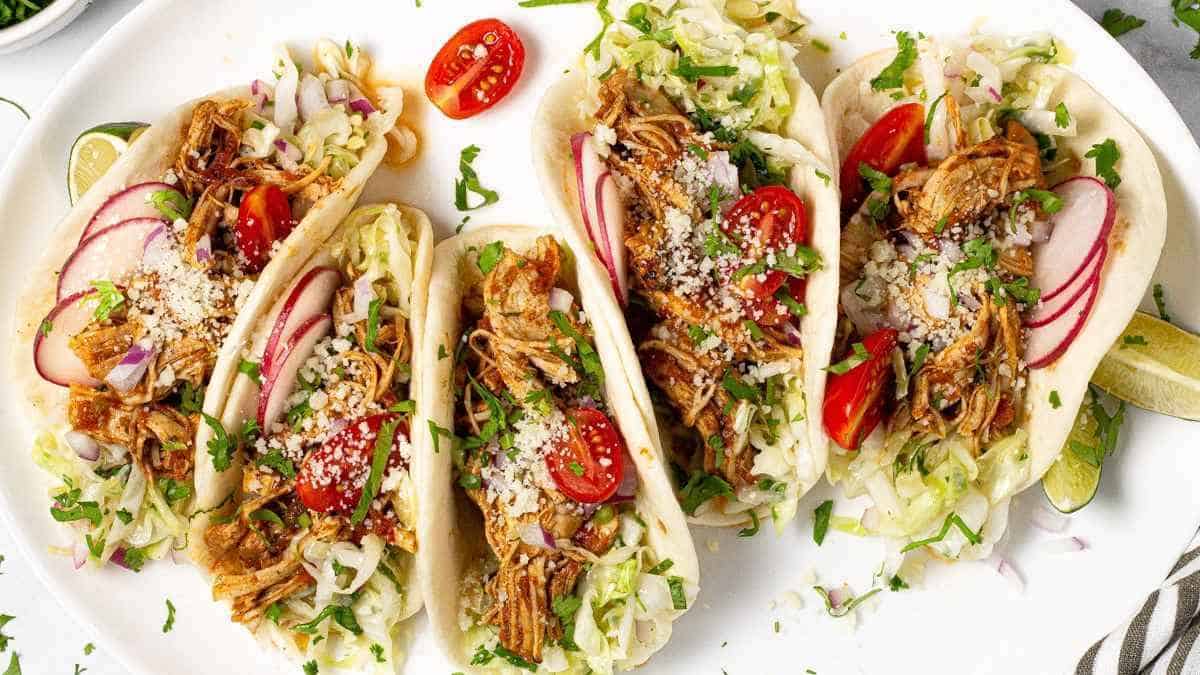 Four pulled pork tacos on a white plate.