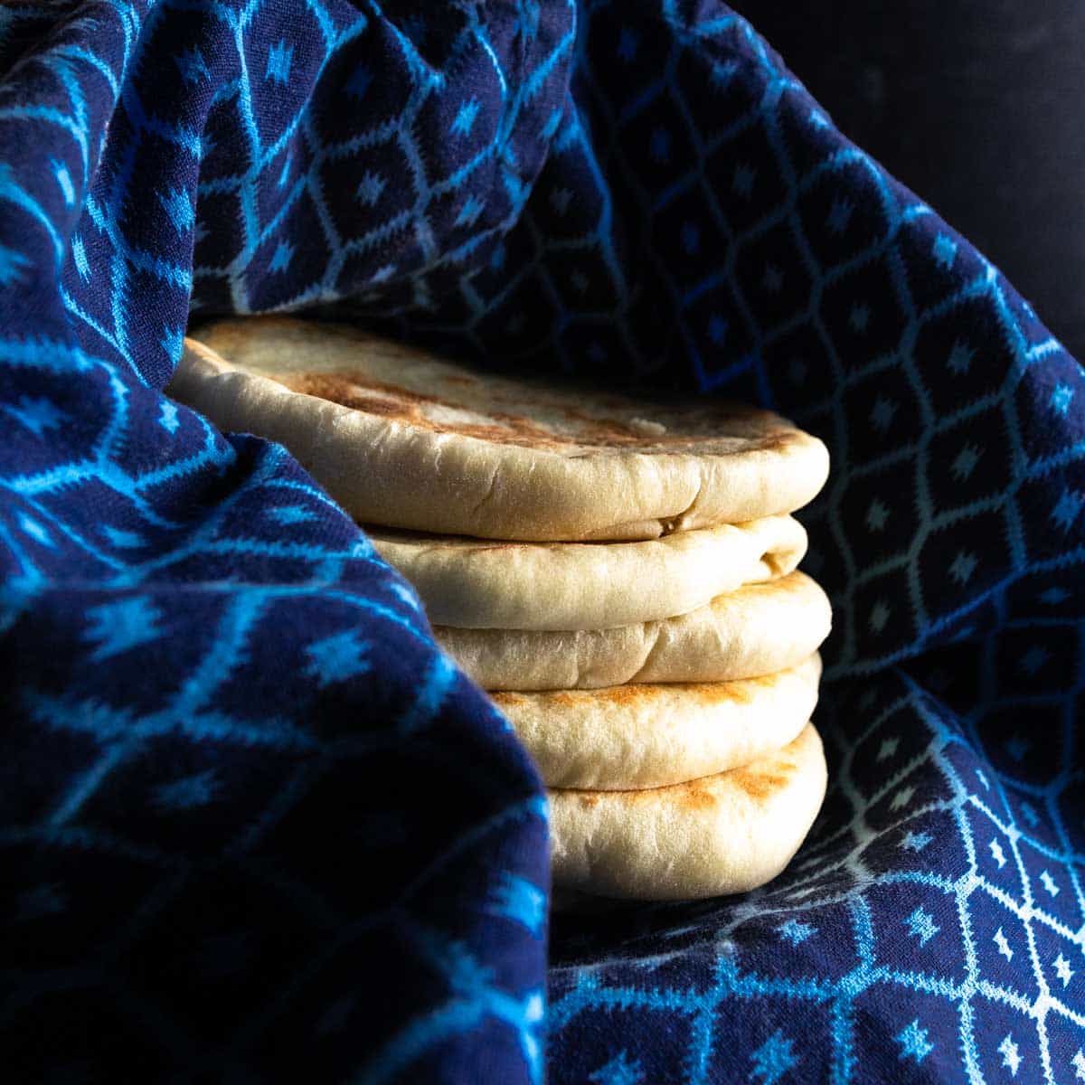 A stack of pita pockets wrapped in a clean dish towel to steam after baking.
