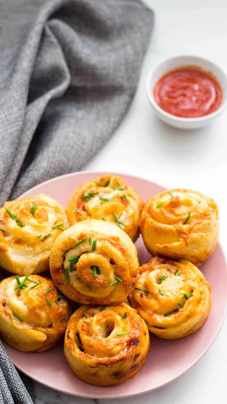 a plate of cooked air fryer pizza rolls ready with a small bowl of marinara sauce.
