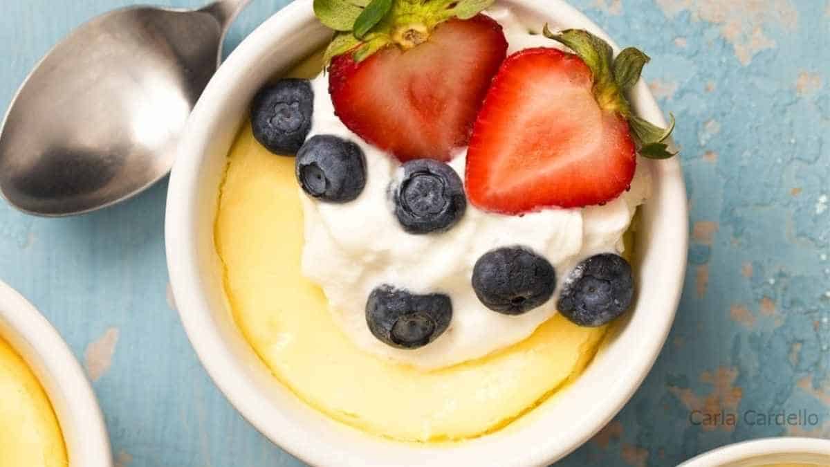 A bowl of lemon pudding with blueberries and whipped cream.