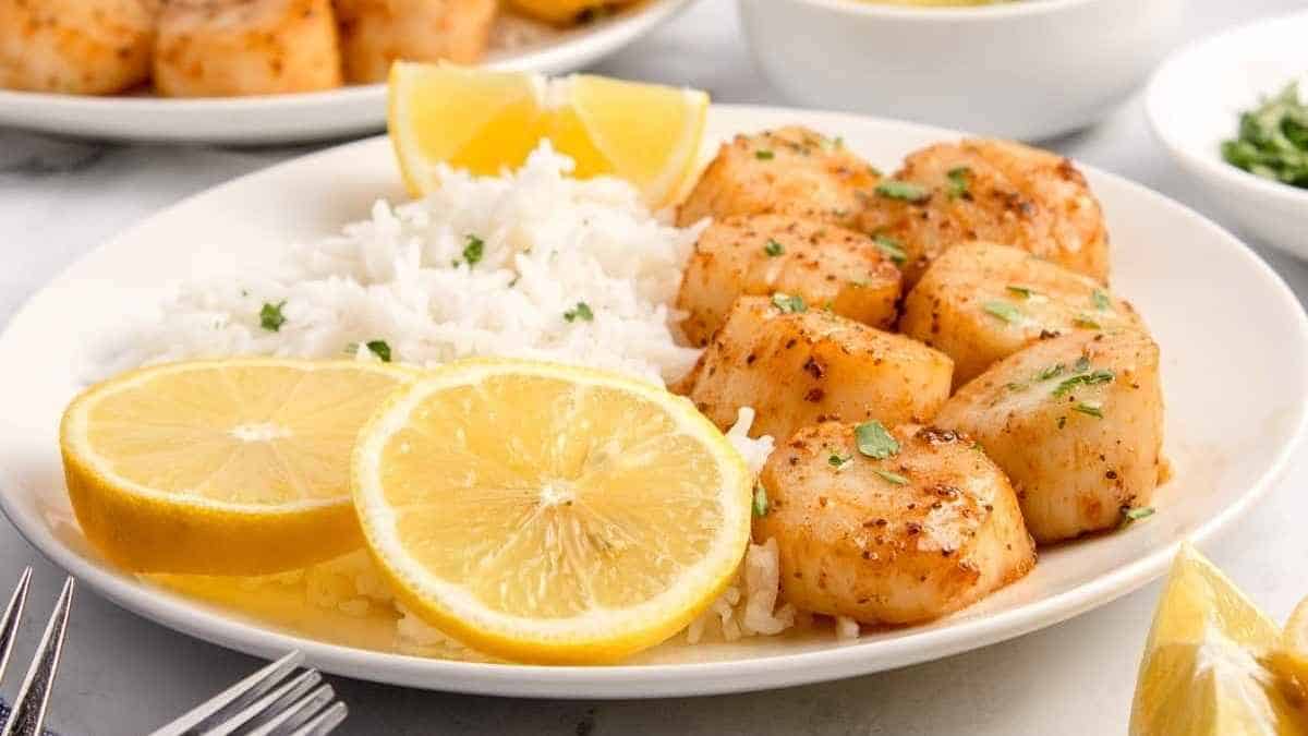 Scallops on a plate with rice and lemon slices.