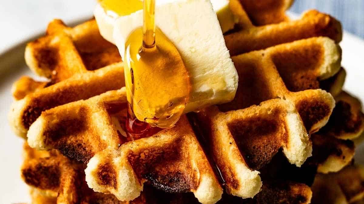 A stack of waffles with honey being poured over them.