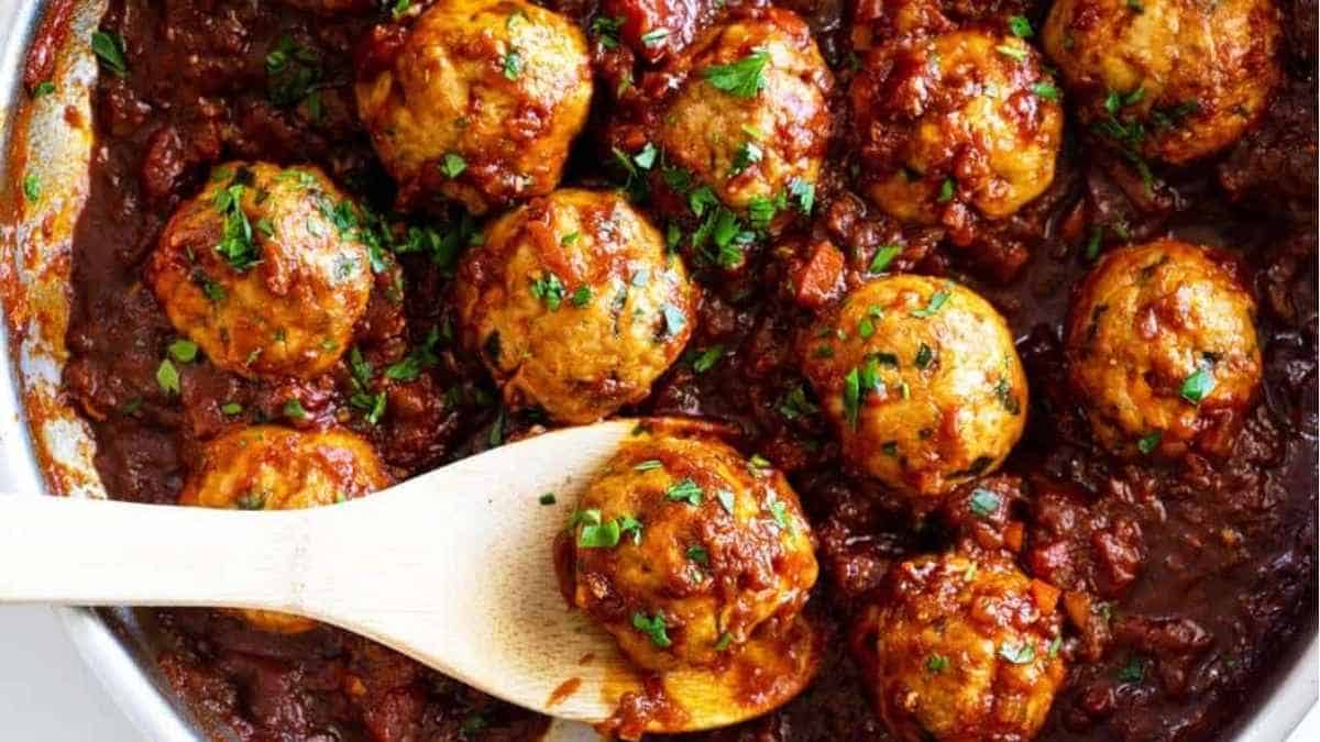 Meatballs in a skillet with a wooden spoon.