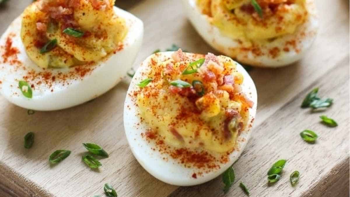Deviled eggs with bacon and chives on a cutting board.