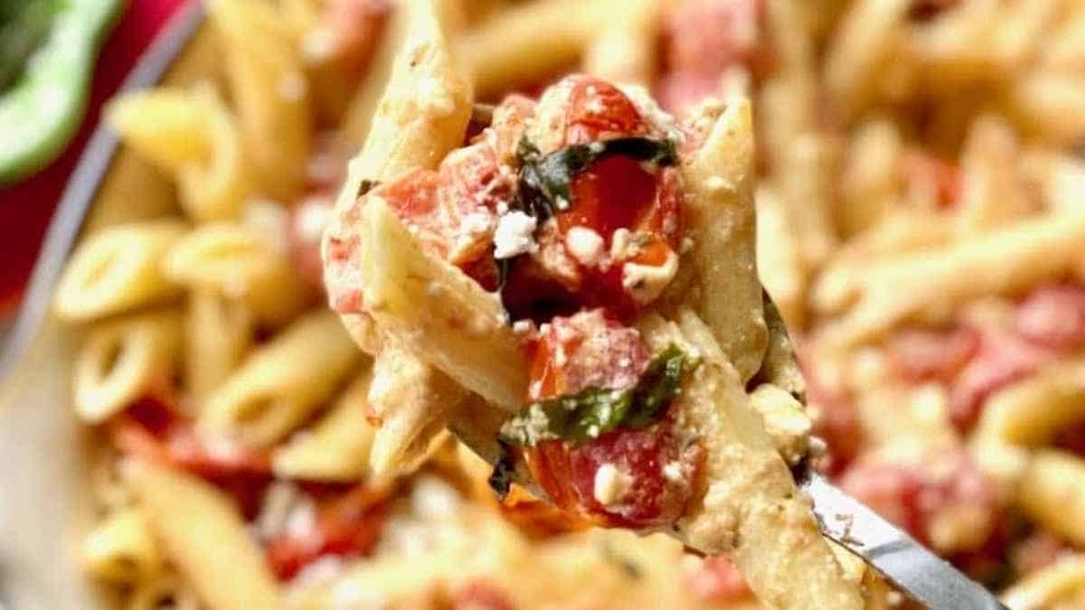 A fork full of pasta with tomatoes and basil.