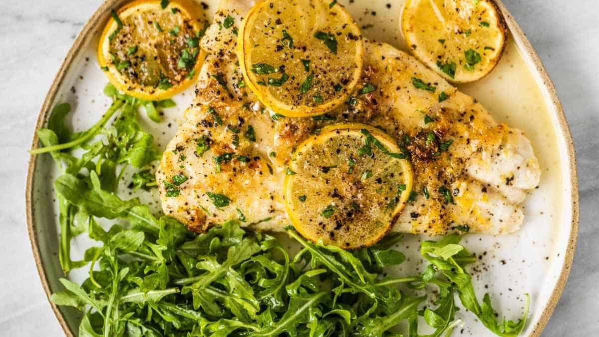Fish fillet with lemon and arugula on a white plate.