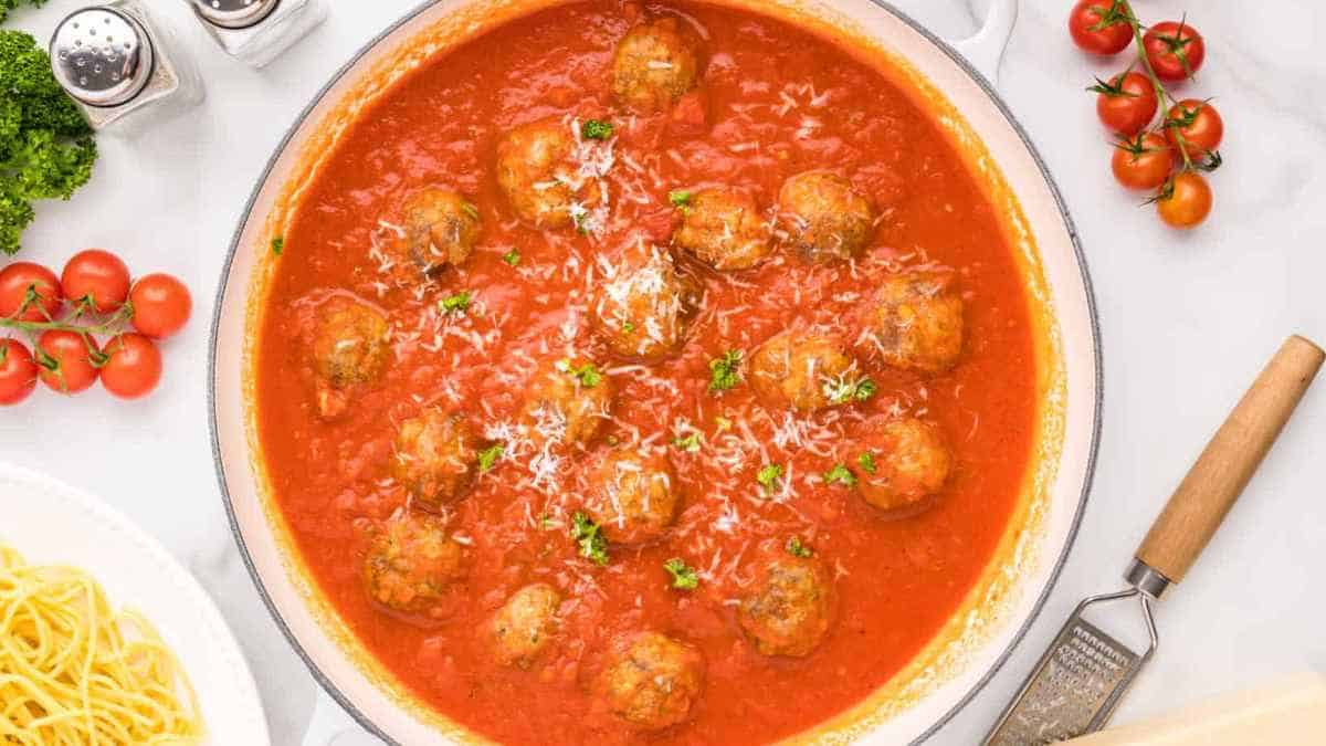 A dish with meatballs and tomatoes on a white table.