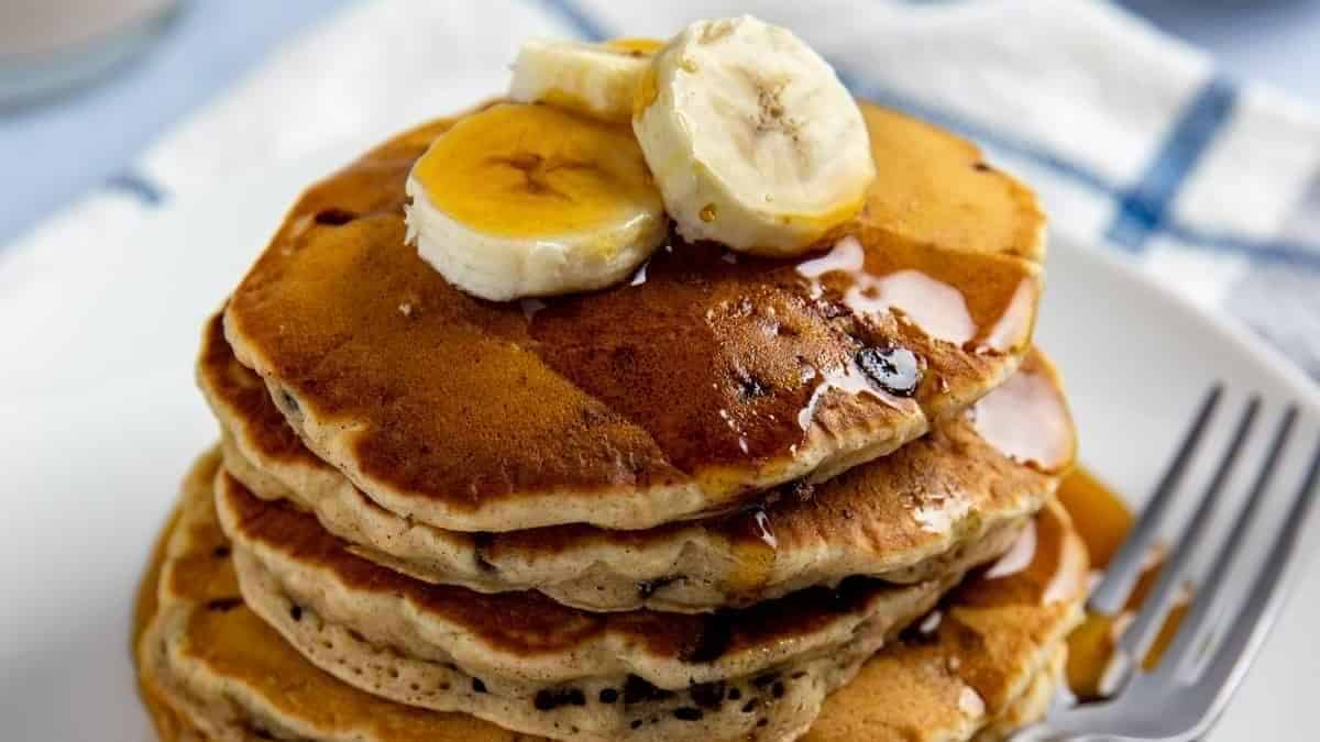 A stack of pancakes with bananas and syrup on a plate.