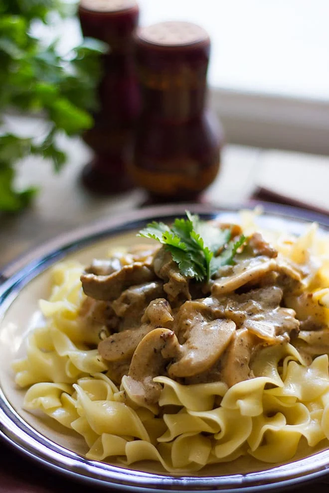 A plate of pasta with shaved beef, mushrooms, and parsley.