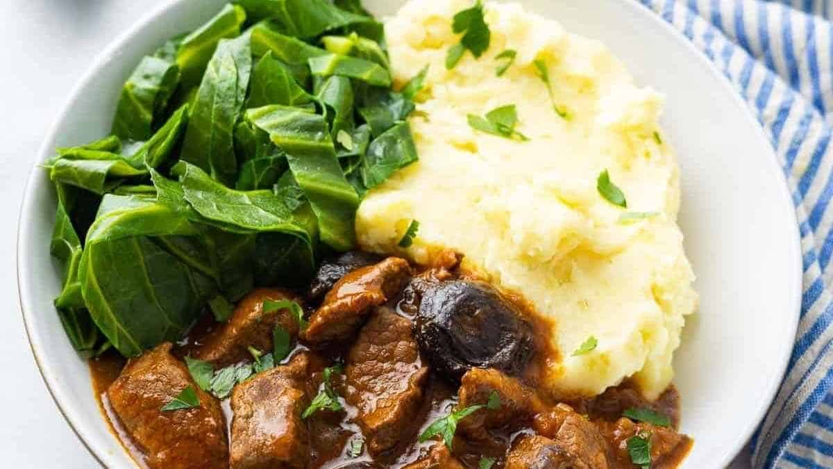 A bowl of beef stew with mashed potatoes and spinach.