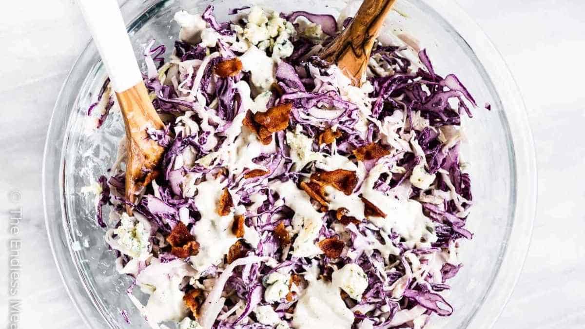 Coleslaw in a glass bowl with wooden spoons.