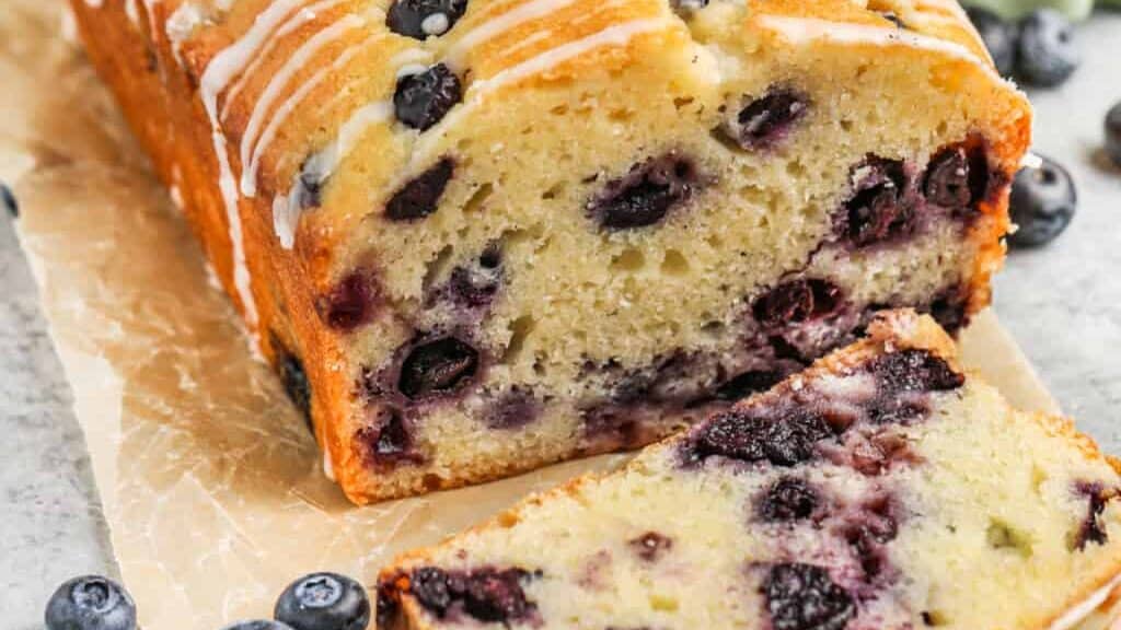 A loaf of blueberry bread with a slice taken out.