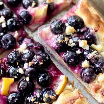 A blueberry and orange pizza on a baking sheet.