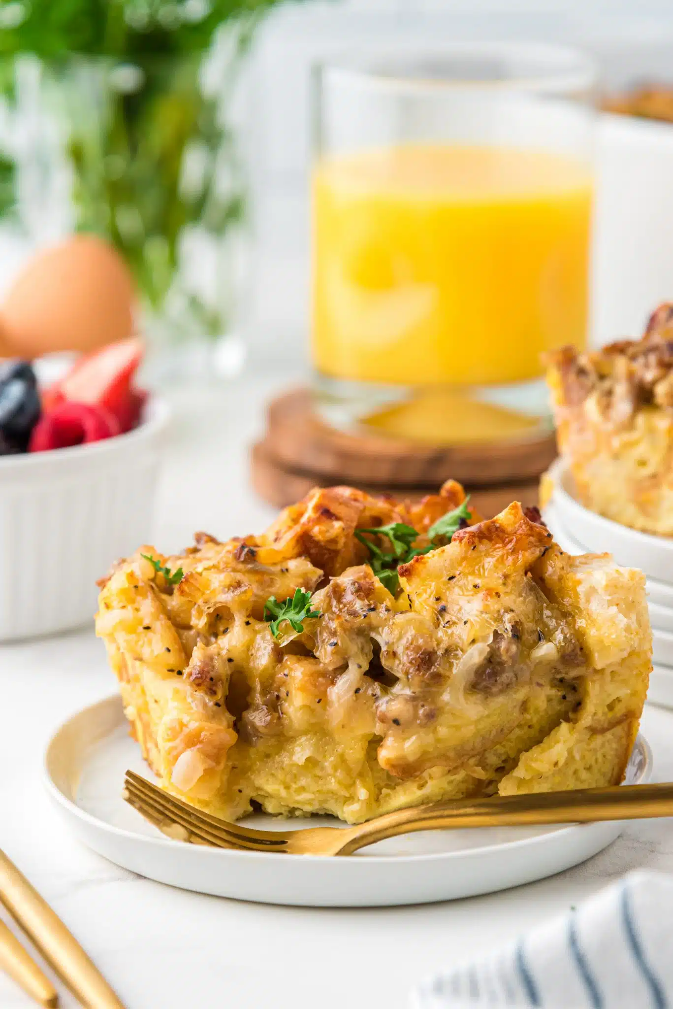 A protein-packed slice of breakfast casserole on a plate next to a cup of refreshing orange juice.