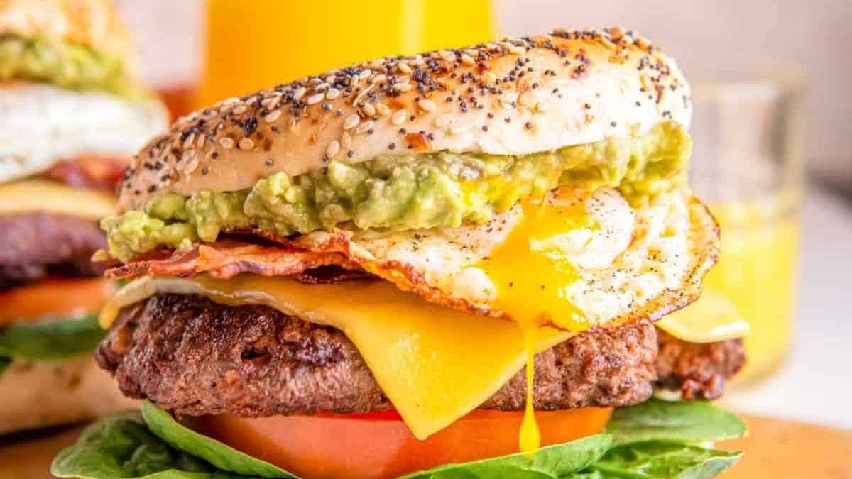 A burger with guacamole, eggs and avocado on a wooden cutting board.