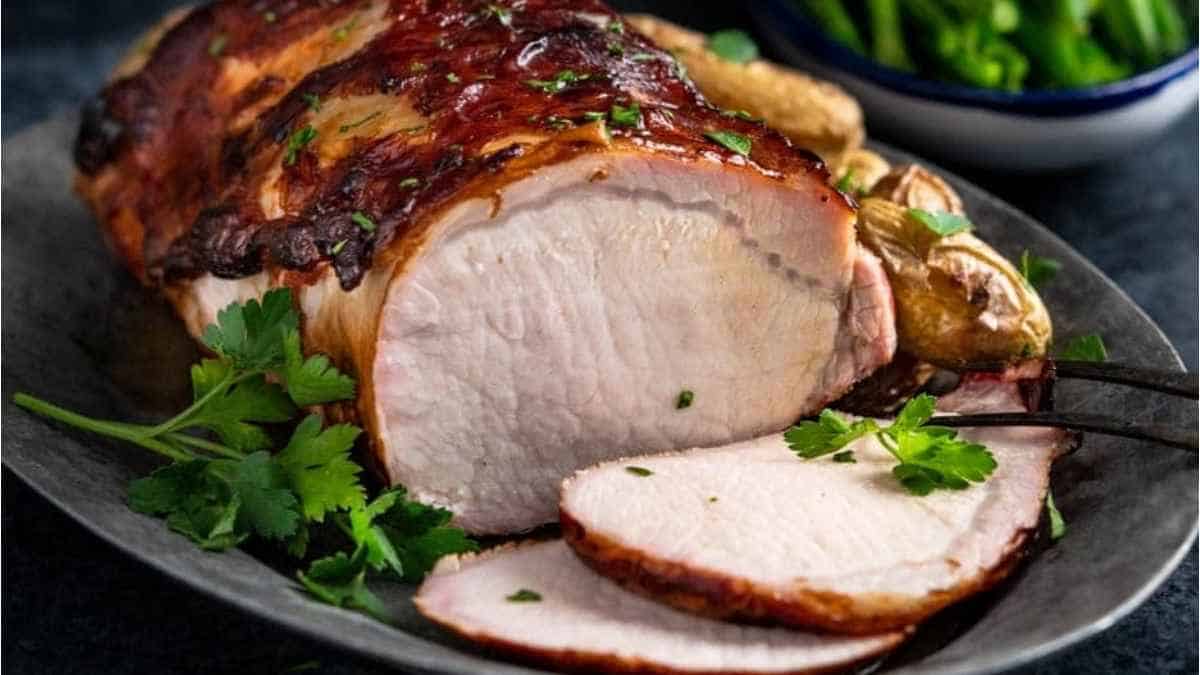 A pork roast on a plate with potatoes and greens.